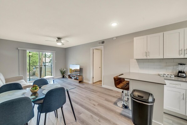 A modern kitchen with white cabinets, a dining area with a glass table, and a view of a balcony.