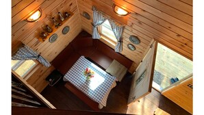 L’intérieur d’un chalet accueillant, avec un plafond en bois, une table à manger recouverte d’une nappe à carreaux et une fenêtre agrémentée de rideaux.