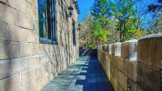 Un chemin de pierre mène à un bâtiment doté de grandes fenêtres et d’un mur de pierre sur un de ses côtés.