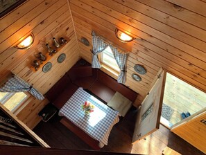 Ein gemütliches Blockhaus-Interieur mit Holzbalkendecke, einem Esstisch mit kariertem Tischläufer und einem fenster mit Vorhängen.