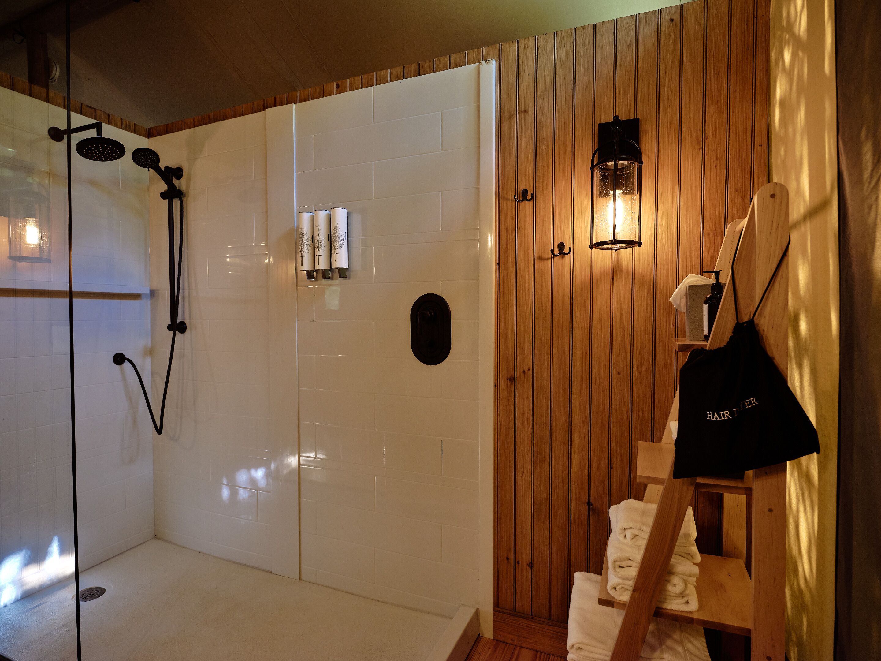 A modern bathroom with a glass-enclosed shower, wooden paneling, a towel rack, and a hairdryer.