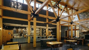 A spacious restaurant with high wooden ceilings, a bar area, and a stone fireplace. - Terramor Outdoor Resort (Bar Harbor)