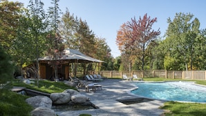 A backyard with a swimming pool, stone patio, lounge chairs, and a wooden cabin. - Terramor Outdoor Resort (Bar Harbor)