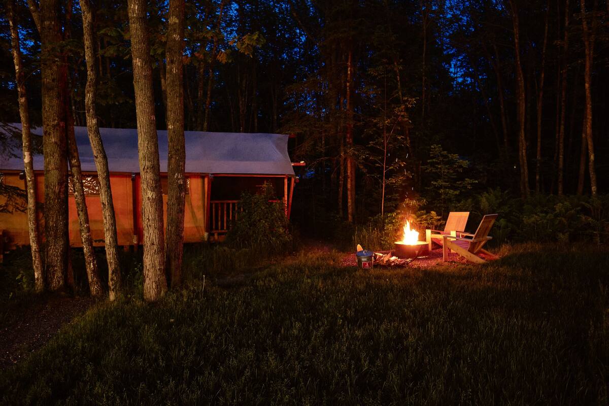 A cabin with a fire pit and chairs in a forested area at night.