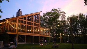 A modern house with large windows and a balcony, surrounded by a grassy yard and trees. - Terramor Outdoor Resort (Bar Harbor)