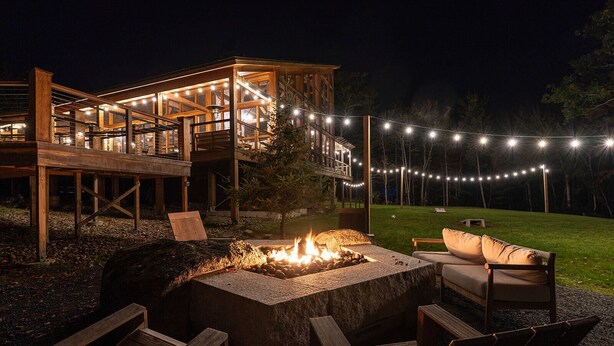 A wooden deck with a fire pit and outdoor seating, surrounded by string lights. - Terramor Outdoor Resort (Bar Harbor)