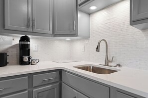A modern kitchen with grey cabinets, a stainless steel sink, and a coffee maker. - Updated Condo Close to Silver Dollar City w Free Tickets-Near Indian Point-Peaceful View! (Branson)