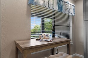 Una habitación con una mesa de madera, una ventana con persianas y vistas al exterior.