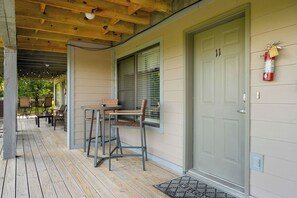 Eine überdachte Veranda mit Tisch und Stühlen, eine Tür mit einer Hausnummer sowie ein an der Wand befestigter Feuerlöscher.