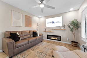 Ein modernes Wohnzimmer mit Ledersofa, Kamin, Wandfernseher und Deckenventilator.