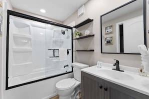 A modern bathroom with a glass-enclosed shower, a white toilet, a sink with a black faucet, and a mirror above the sink.