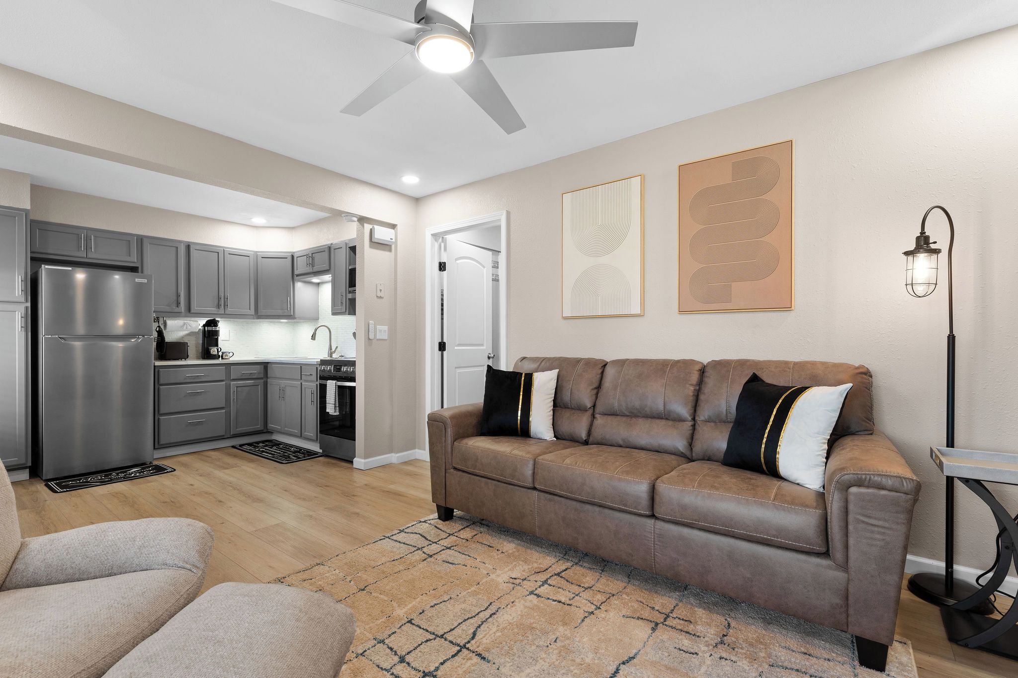 A modern living room with a brown leather sofa, a dining area, and a kitchen with grey cabinets.