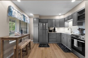 Eine moderne Küche mit grauen Schränken, einem Edelstahlkühlschrank, einer Kaffeemaschine und einem Holztisch mit zwei Hocker.