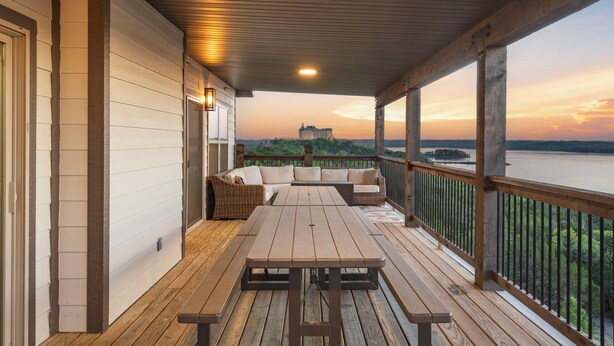Une terrasse couverte, avec une table et des bancs en bois, d’où l’on peut admirer une rivière et un bâtiment situé au loin.