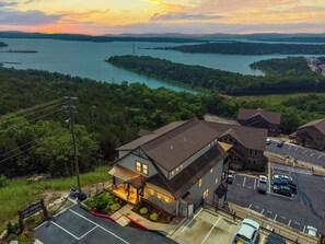 A hotel with a parking lot, a view of a lake, and a forested area.