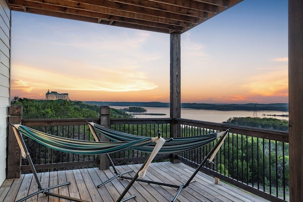 A wooden deck with two hammocks overlooking a body of water and a distant building.