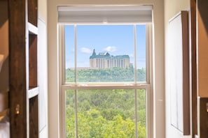 A window with a view of a large building surrounded by trees.