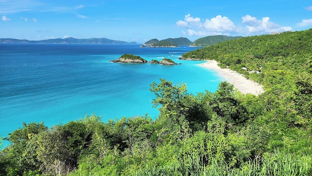 Paesaggio costiero con acque turchesi cristalline, una spiaggia sabbiosa e vegetazione lussureggiante.
