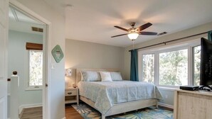Un dormitorio con cama, ventilador de techo, mesita de noche, cómoda y ventana con cortinas.