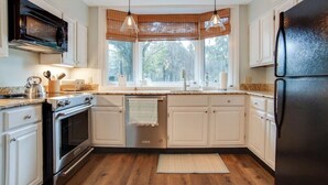 Una cocina moderna con armarios blancos, un refrigerador negro, una estufa y una ventana con vista a árboles.