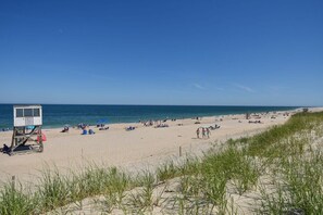 Una playa con una torre de salvavidas, arena y dunas cubiertas de hierba.
