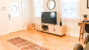 Ett vardagsrum med en tv p å ett träställ, ett litet bord med en växt och en dörr som är dekorerad med en krans.