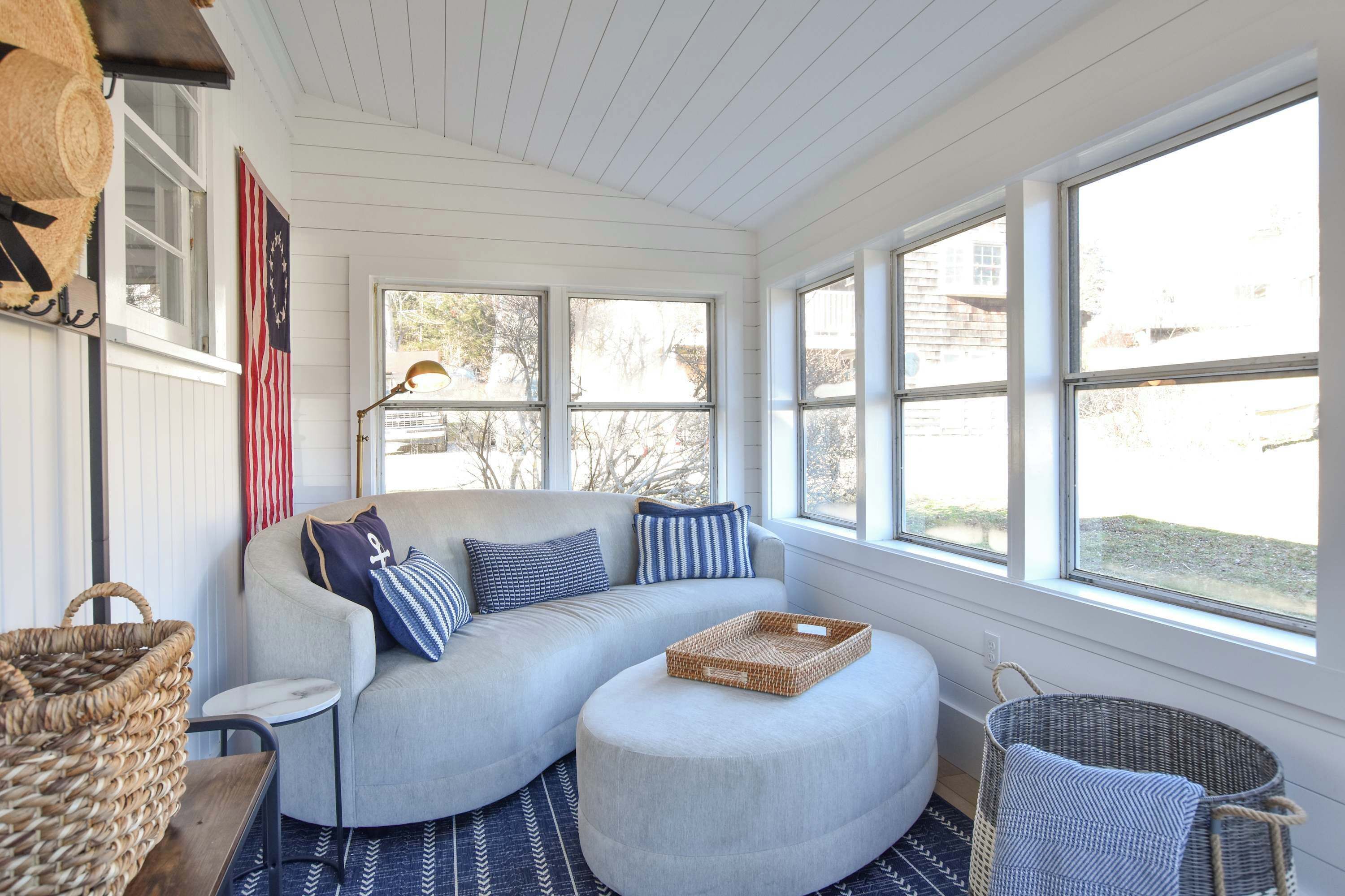 A cozy room with a curved gray sofa, a round ottoman, and a wicker basket.