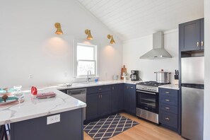 Une cuisine moderne avec des meubles de couleur sombre, un plan de travail blanc, une cuisinière à gaz, un réfrigérateur en acier inoxydable et des luminaires suspendus.