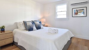 Une chambre à coucher comprenant un lit, une table de chevet, une lampe, un climatiseur fixé au mur et un tableau encadré.