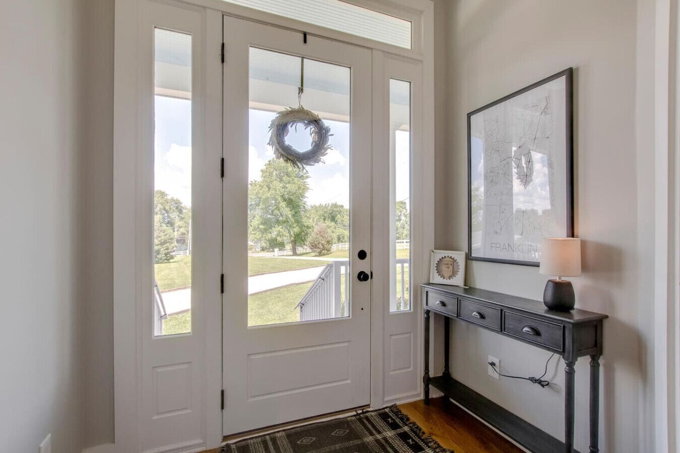 A front door with a wreath, a framed map, and a lamp on a console table.