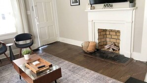 A living room with a fireplace, a television mounted above it, and a coffee table with a remote control. - Cozy Historic Oakwood Duplex (Raleigh)