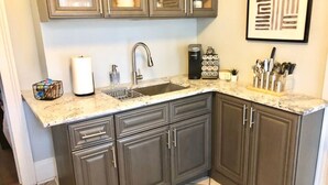 A kitchen with dark cabinets, a granite countertop, a stainless steel sink, and a coffee maker. - Cozy Historic Oakwood Duplex (Raleigh)