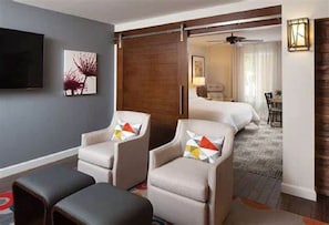 Una habitación de hotel con cama, dos sillones, un televisor y un cuadro en la pared.