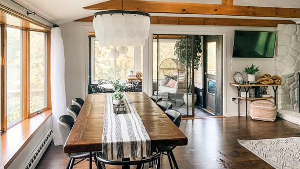 Uma ampla sala de jantar com uma longa mesa de madeira, cadeiras pretas e um lustre branco.