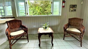 A room with two wicker chairs, a small table with a plant, a window with shutters, and a fire extinguisher on the wall. - Grand Chalet,  Private Pool, AC, River Access, Pool Table BBQ WIFI Parking (Rio Grande)