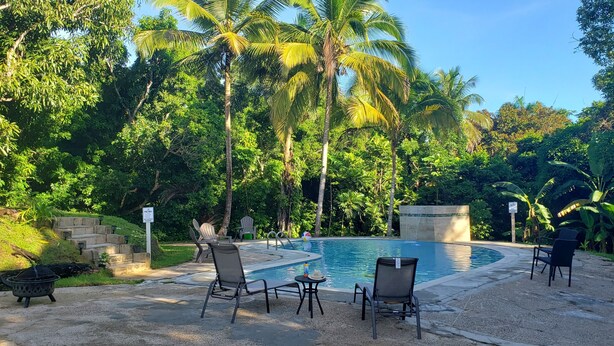 A pool area with lounge chairs and a small table, surrounded by lush greenery and palm trees. - Grand Chalet,  Private Pool, AC, River Access, Pool Table BBQ WIFI Parking (Rio Grande)