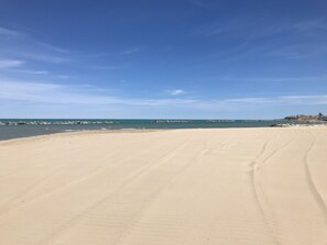 Una playa amplia de arena con cielo azul despejado y mar tranquilo.