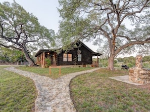 Escape to a serene log cabin surrounded by nature, featuring a cozy entrance with a bench and a traditional pitched roof.