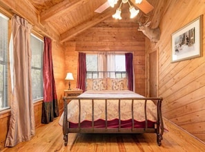 Cozy cabin-style bedroom with a single bed, wooden ceiling, and a framed picture on the wall.