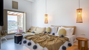 A modern bedroom with a bed, bedside tables, a sofa, and a view through a large window. - Due Mari Mykonos (Mykonos)