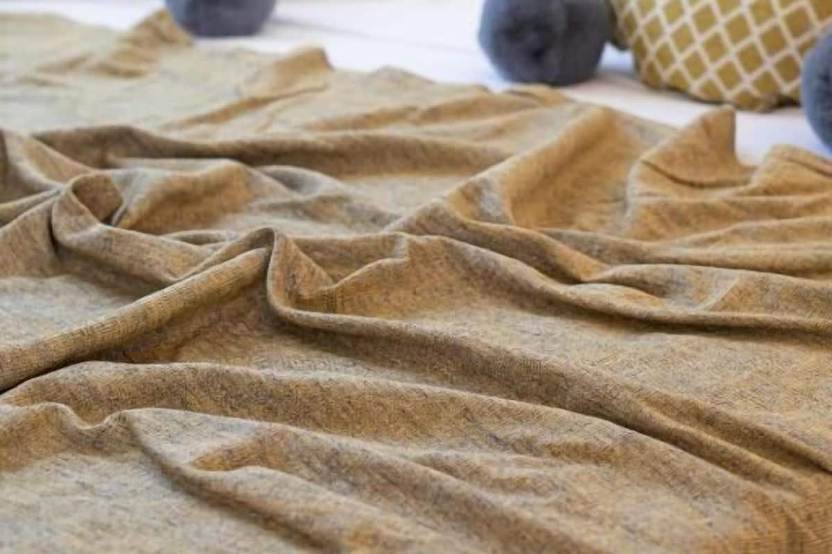 Cama com manta bege, almofadas brancas e mantas estampadas.