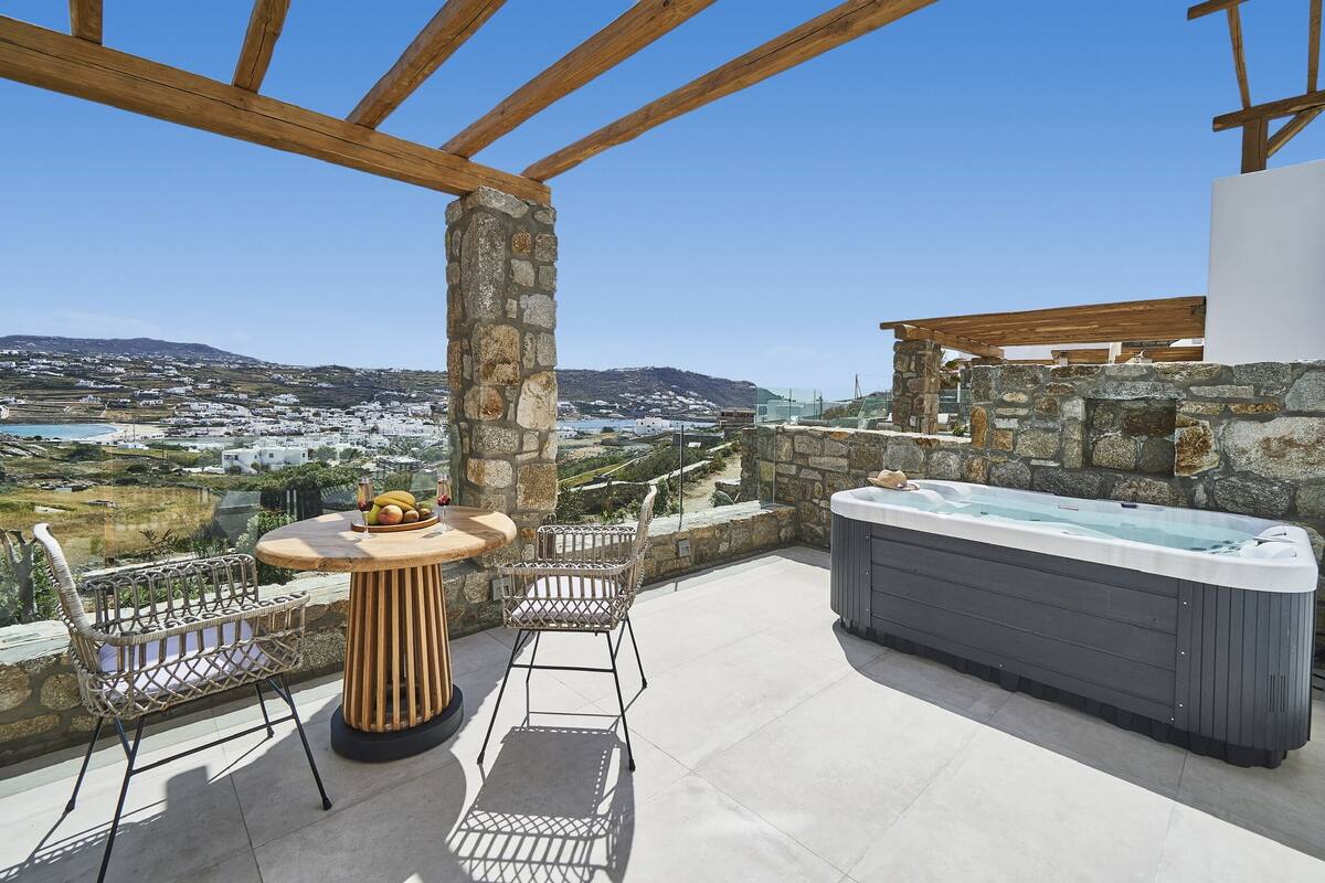 Um terraço no telhado com um pilar de pedra, uma mesa de madeira com cadeiras e uma banheira de hidromassagem.