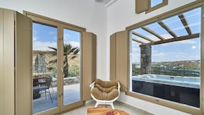 A room with large sliding glass doors, a white chair, a wooden table with apples, and a view of a hot tub and landscape. - Due Mari Mykonos (Mykonos)