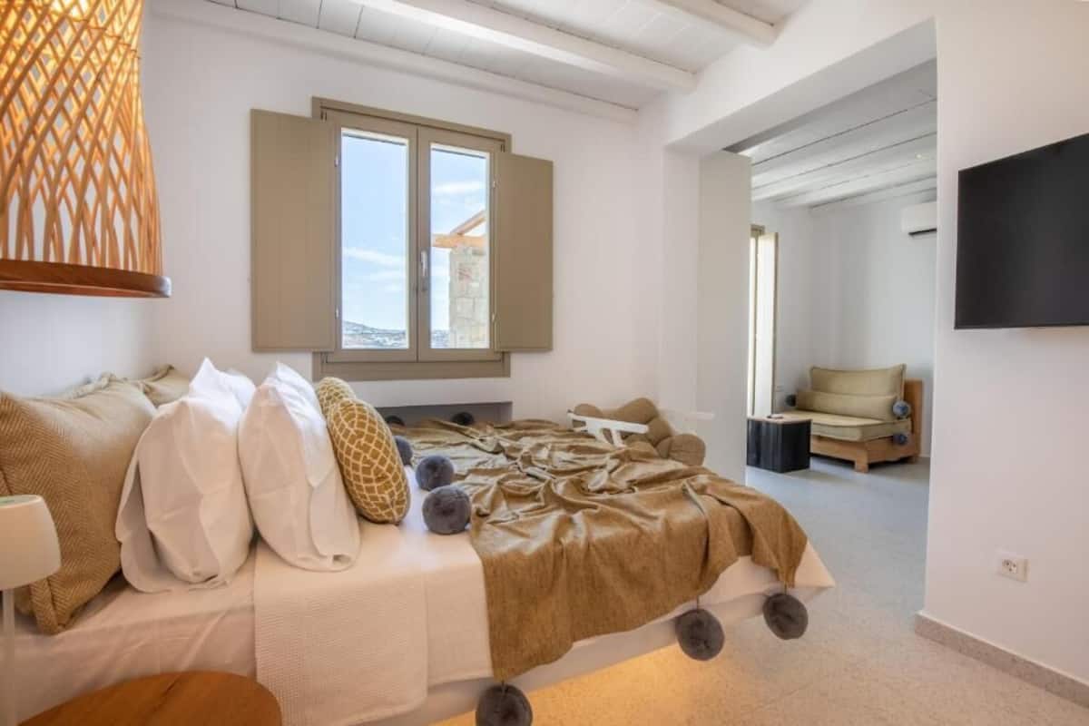 Quarto moderno com cama, janela, televisão e vista para o exterior.