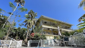 A two-story building with balconies, a swimming pool, and surrounding palm trees.