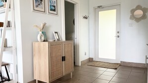 A hallway with a wooden cabinet, framed pictures on the wall, a white door, and a tiled floor.