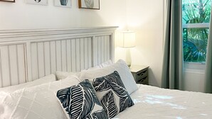 A bedroom with a bed, a headboard, a nightstand, a lamp, and a window with curtains.