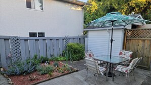 Een terras met een tafel en stoelen, omgeven door een tuin met diverse planten en een houten hek.