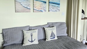 Ein Schlafzimmer mit einem Bett, zwei Kissen und drei an der Wand befestigten Bildern, die eine Strandansicht zeigen.
