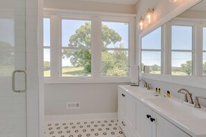 A bathroom with a large window, a white sink, and a mirror.